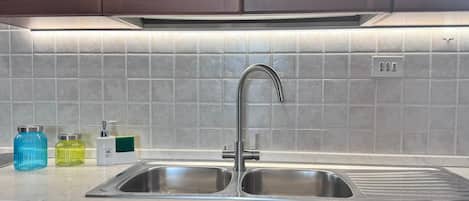 A kitchen with a double sink, wooden cabinets, and a tiled backsplash.