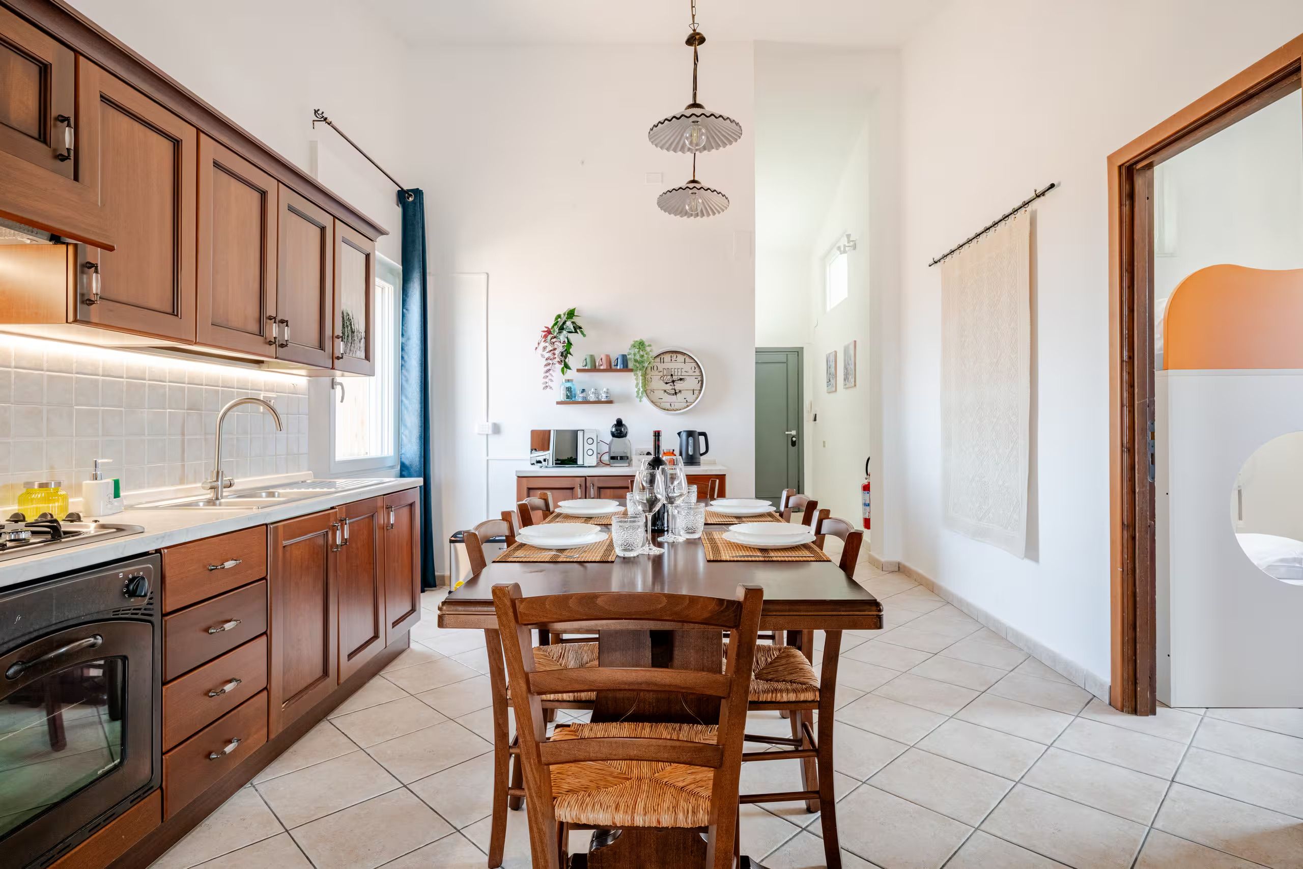 Een moderne keuken met houten kastjes, een inbouwoven en een eethoek met een tafel voor vier personen.