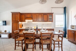 A modern kitchen with wooden cabinets, a dining table set for six, and a large window with curtains.