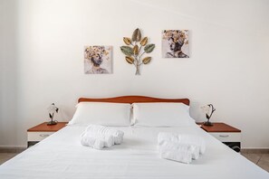 A hotel room with a large bed, two nightstands, and three wall-mounted artworks. - Sardinia. Cozy apartment in the city center with a balcony and panoramic views. Serves 6. (Tortolì)