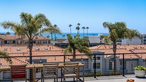 Una terrazza con vista sul mare, palme e edifici con tetti in tegole rosse.