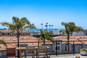 Eine Terrasse mit Blick auf das Meer, Palmen und Gebäude mit roten Ziegeldächern.