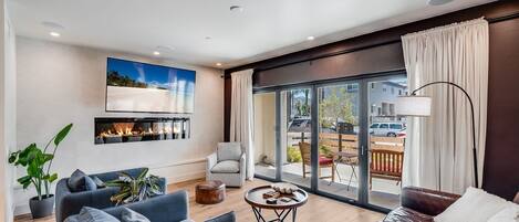 A modern living room with a fireplace, a large TV, and a view of the outside.