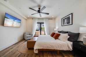 Ein Schlafzimmer mit einem Bett, einem Deckenventilator, einem Fernseher, einem Sessel, einem Nachttisch und Blick ins Freie.