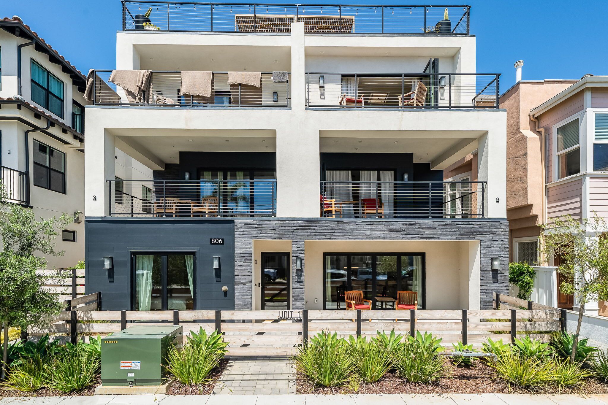 A modern multi-story residential building with balconies, a covered entrance, and a small outdoor seating area.