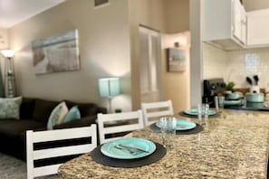 A dining area with a granite countertop, white chairs, and a table set with plates, glasses, and cutlery. - Airport & Stadium Hub with Coastal Vibes and Patio (Tampa)