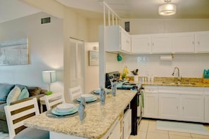 A kitchen with white cabinets, a granite countertop, and a dining area with a table set for four. - Airport & Stadium Hub with Coastal Vibes and Patio (Tampa)