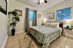 A bedroom with a bed, a ceiling fan, a window with blinds, a potted plant, and artwork on the walls. - Airport & Stadium Hub with Coastal Vibes and Patio (Tampa)