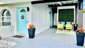 Ein modernes Haus mit einer hellblauen Tür, einer Veranda mit gelben Stühlen und einer grünen Wand.