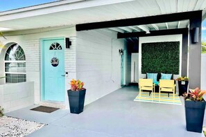 Ein modernes Haus mit einer hellblauen Tür, einer Veranda mit gelben Stühlen und einer grünen Wand.