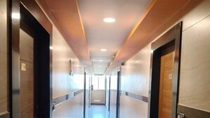 A long, narrow hallway with doors on both sides, a tiled floor, and recessed lighting on the ceiling. - orange elite stays white field (Bengaluru)
