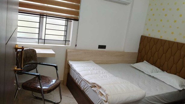 A bedroom with a bed, a desk, a chair, an air conditioning unit, and a window with blinds. - orange elite stays white field (Bengaluru)