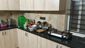 A kitchen with wooden cabinets, a gas stove, and various kitchen utensils. - orange elite stays white field (Bengaluru)