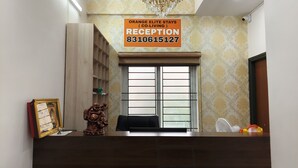 A reception desk with a chandelier, a reception sign, and a window with blinds. - orange elite stays white field (Bengaluru)