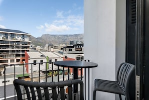 Een balkon met een tafel en stoelen, met uitzicht op een stadsgezicht met gebouwen en bergen in de verte.