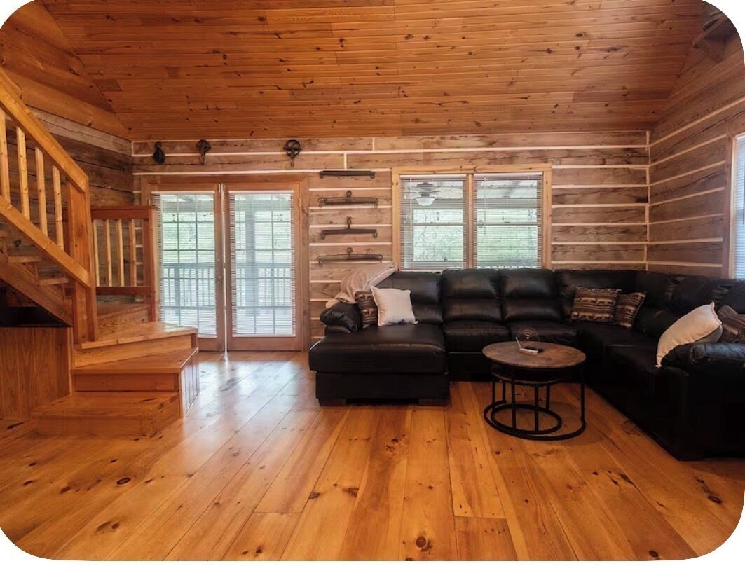 Un interior de madera con una escalera, un sofá de cuero negro y una mesa de centro redonda.