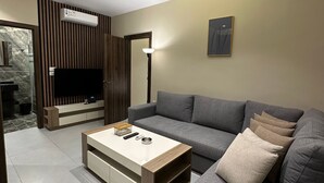 A modern living room with a grey sofa, a white coffee table, and a flat-screen TV mounted on a wooden panel. - 301 Al-najeh JRE Apartments For Rent ave (Amman)