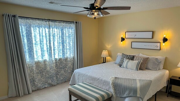 A bedroom with a large bed, a ceiling fan, two wall-mounted lamps, and a window with curtains. - Welcome to Royale Retreat at Pointe Royal, in Branson, Missouri! (Branson)