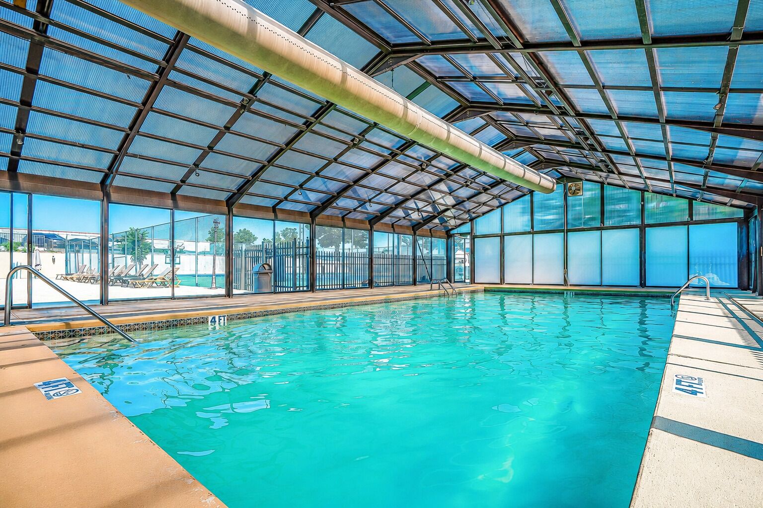 Une piscine intérieure avec des parois en verre transparent, un toit en métal et une vue sur la plage.