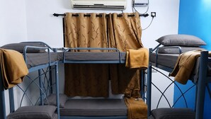A bunk bed room with a woven stool, a wall-mounted air conditioner, and a curtain. - Meriton Stays  Anna Nagar Bed in 6-Bed Male AC Dorm Free Wi-Fi (Chennai)