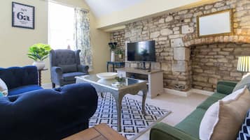Ein Wohnzimmer mit Steinwand, einem Fernseher und Möbeln, darunter ein blaues Sofa, ein grünes Sofa und ein grauer Sessel.
