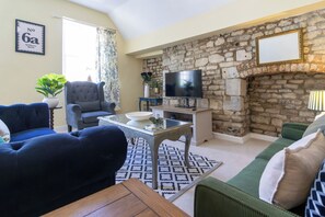 Una sala de estar con una pared de piedra, un televisor y muebles que incluyen un sofá azul, un sofá verde y un sillón gris.