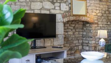 A stone wall with a flat-screen TV, a small table with a lamp, and a bowl on a shelf.