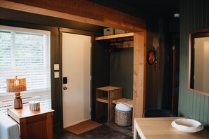 A room with a wooden door, a small table with a lamp, a wicker basket, and a wooden shelf with boxes. - Petit Lodge | Ski-In/Ski-Out Tremblant (Mont-Tremblant)