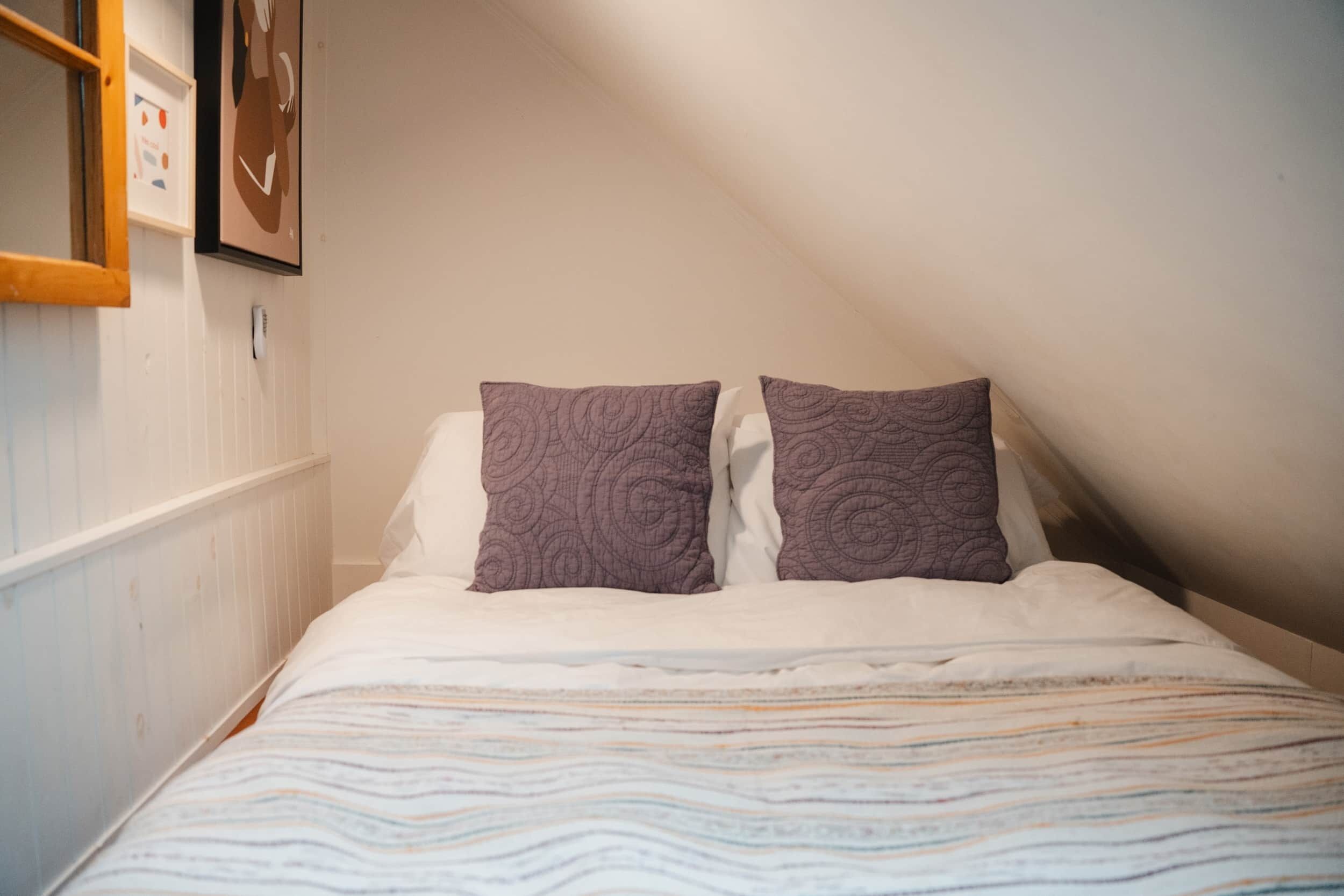 Ein Schlafzimmer mit schrägverdeckter Decke, weißen Wänden und einem Bett mit gemustertem Bettbezug.
