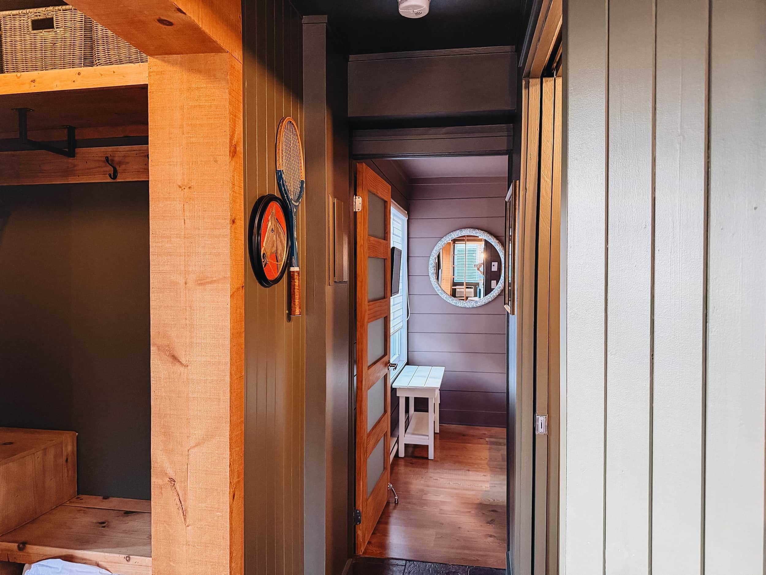 Een smalle gang met houten wanden, een witte bank en een ronde spiegel aan de rechterkant.
