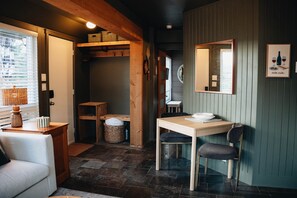A cozy room with a wooden table, a chair, a sofa, and a window with blinds. - Petit Lodge | Ski-In/Ski-Out Tremblant (Mont-Tremblant)