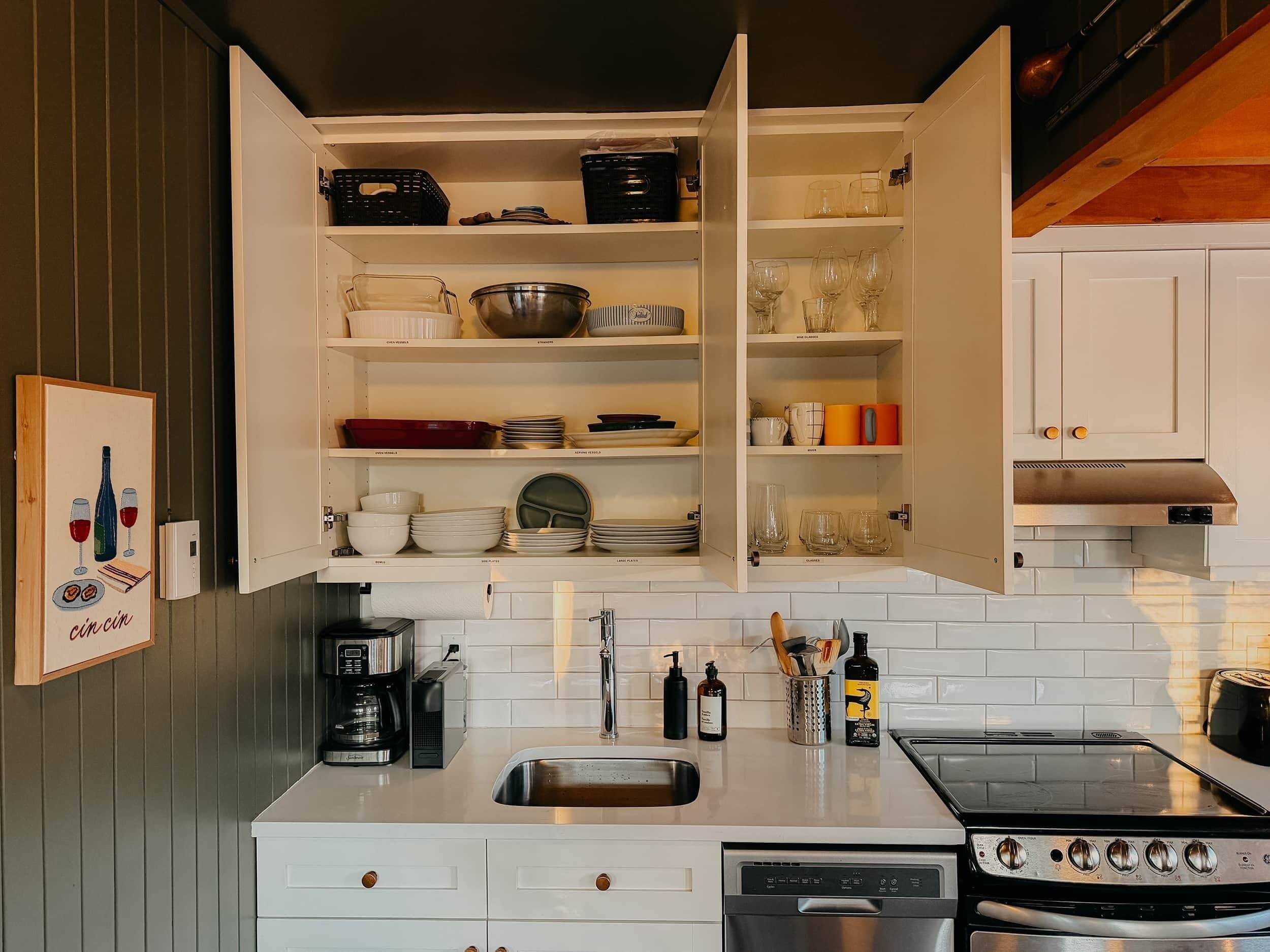 Una cocina con armarios blancos, un lavamanos de acero inoxidable, una cafetera y una estufa.