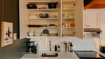 Una cocina con armarios blancos, un lavamanos de acero inoxidable, una cafetera y una estufa.