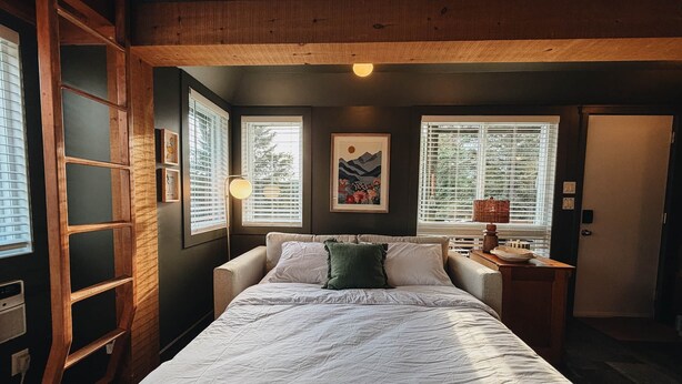 Un dormitorio con cama, mesita de noche, lámpara y ventana con persianas.
