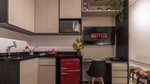 A modern kitchen with a red Philco refrigerator, a black countertop, and a dining area with a chair and table. - StayHome VN Turiassu | Gym & Pool by Allianz Parque (São Paulo)