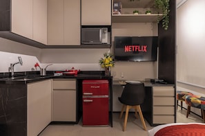 A modern kitchen with a red Philco refrigerator, a black countertop, and a dining area with a chair and table. - StayHome VN Turiassu | Gym & Pool by Allianz Parque (São Paulo)