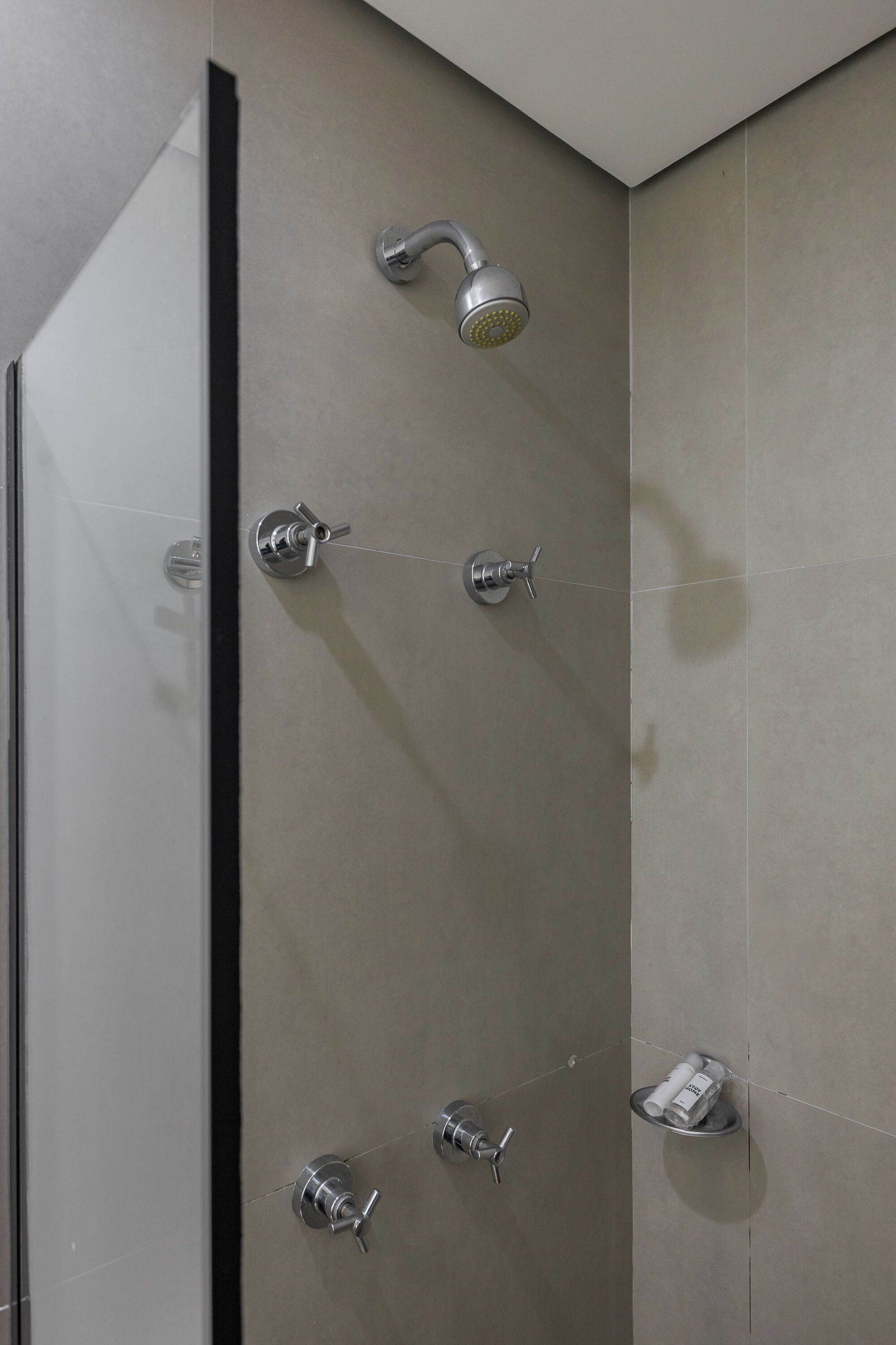 A shower with multiple heads and a small shelf with toiletries.