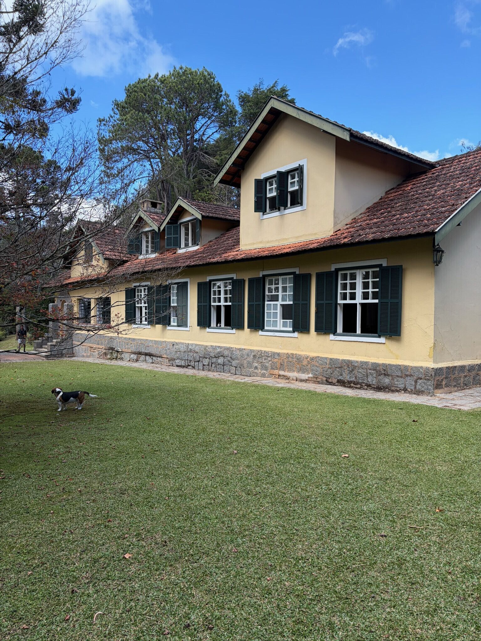 Un edificio de dos pisos con base de piedra, varias ventanas con contraventanas y un césped bien cuidado.