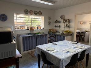 A kitchen with a dining area, a window with a view of greenery, and various kitchen utensils and appliances. - Historic Mansion with Fireplace in Campos do Jordão (Campos do Jordão)