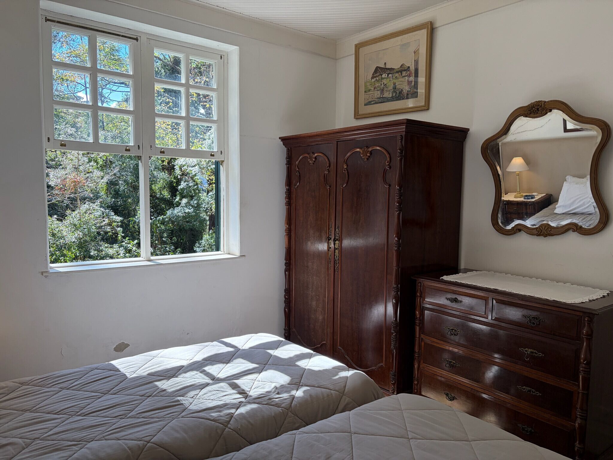 Ein Schlafzimmer mit einem Bett, einem Schminktisch, einem Spiegel und einem Fenster mit Blick auf Bäume.