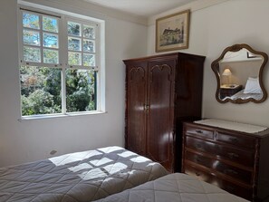 A bedroom with a bed, a dresser, a mirror, and a window with a view of trees. - Historic Mansion with Fireplace in Campos do Jordão (Campos do Jordão)