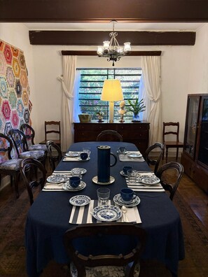 Ein Esszimmer mit Tisch für vier Personen, mit blau-weißem Geschirr, einer blauen Karaffe und einer darüber hängenden Leuchter.