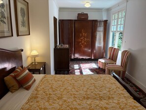 Et hotelværelse med en seng, en stol, et lille bord med lampe, et klædeskab og et vindue med udsigt.