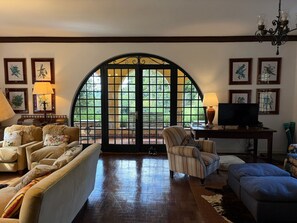 A living room with a large arched window, a television, and various framed artworks on the walls. - Historic Mansion with Fireplace in Campos do Jordão (Campos do Jordão)
