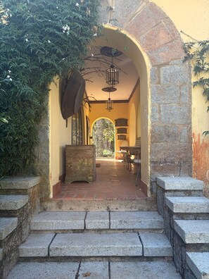 A stone staircase leading to an arched doorway with a lantern above, surrounded by greenery. - Historic Mansion with Fireplace in Campos do Jordão (Campos do Jordão)