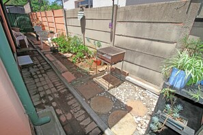 A garden area with a brick pathway, potted plants, and a metal bird feeder.