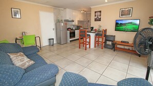 Un espacio habitable compacto con kitchenette, comedor y zona de estar con sofá y sillas.