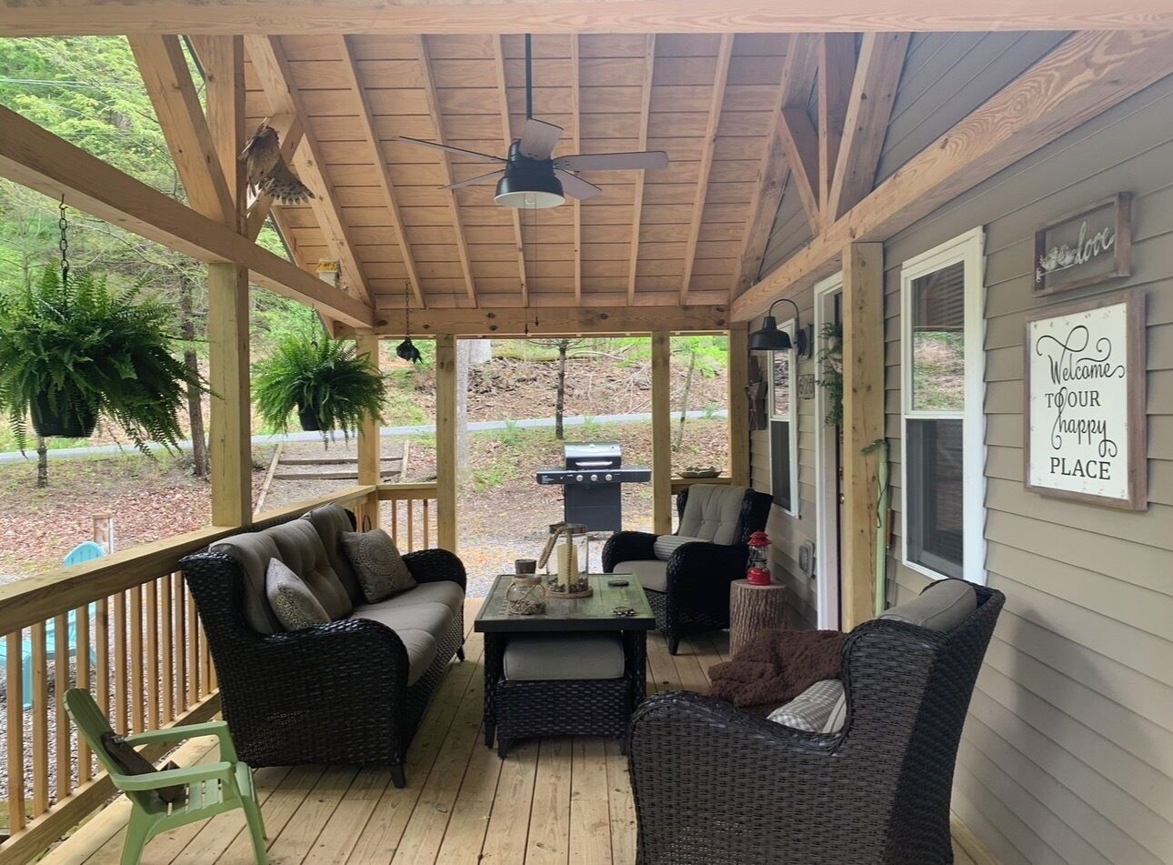 A covered porch with wicker furniture, a ceiling fan, and a 'Welcome to our happy place' sign.