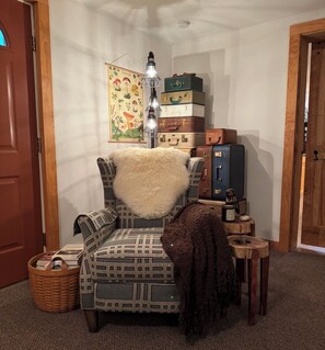A corner room with a patterned armchair, a lamp, stacked suitcases, a small table with a bottle, and a wall with a poster. - Crooked Riffles. Adult only sanctuary nestled above the Loyalsick Creek. (Montoursville)