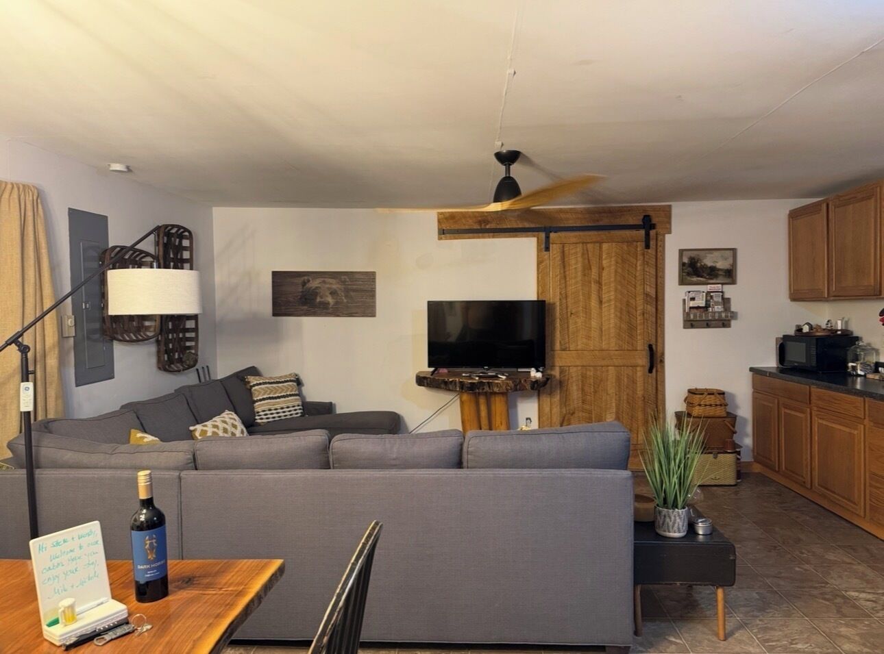 A living room with a sofa, a television, a wooden cabinet, and a dining table with a bottle.